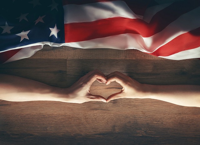 Hände formen ein Herz vor der amerikanischen Flagge, ein Symbol für die starke Freundschaft und Zuneigung zwischen Frankreich und den USA.